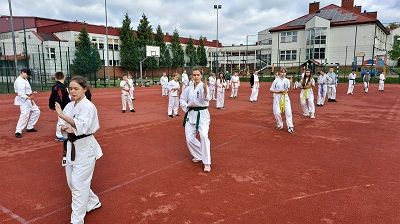 Fotografia przedstawiająca karateków z Akademii Karate Szydłowiec na boisku szkolym, podczas zajęć na świeżym powietrzu.