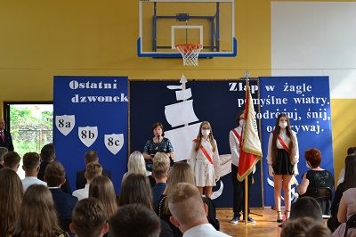 Zakończenie roku szkolnego, Danuta Gnat wygłasza przemowę. W tle sztandar szkoły i napis "Żegnaj * klaso"